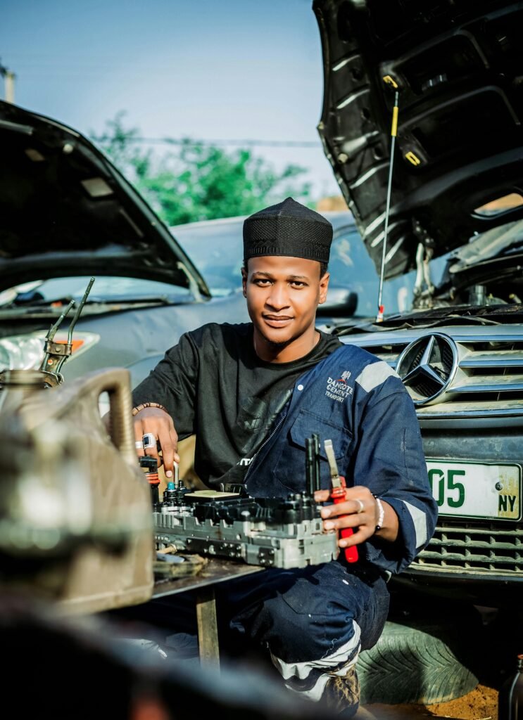 Young mechanic wearing uniform repairs a car outdoors, showcasing expertise in automotive service.