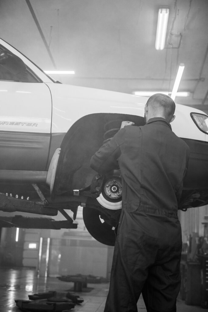 A mechanic fixing a car in an indoor repair shop setting, black and white photo.