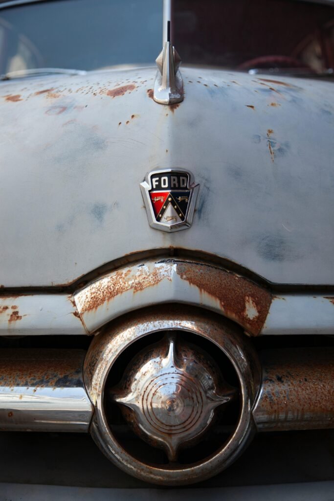 Detailed shot of a rusted vintage Ford car emblem and grille, showcasing classic automotive charm.