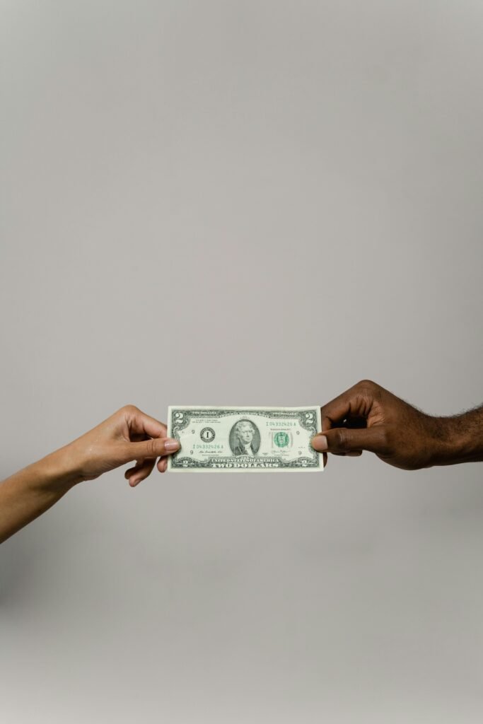 A dollar bill is exchanged between two diverse hands on a neutral background.